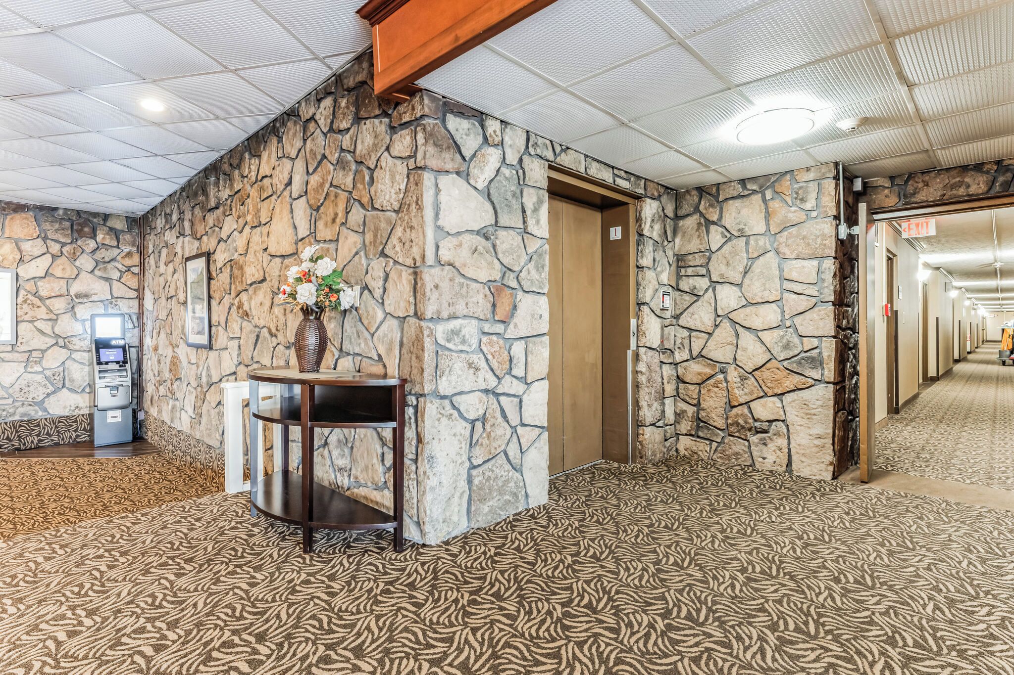 A lobby with a stone wall, a reception desk, a flower vase, and a carpeted floor.