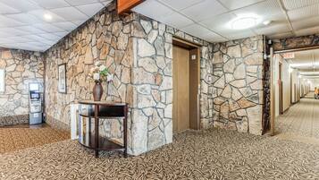 A lobby with a stone wall, a reception desk, a flower vase, and a carpeted floor.