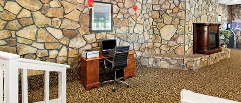 Un hall d’entrée avec un mur en pierre, un bureau en bois avec un ordinateur, un banc blanc et une moquette à motifs.