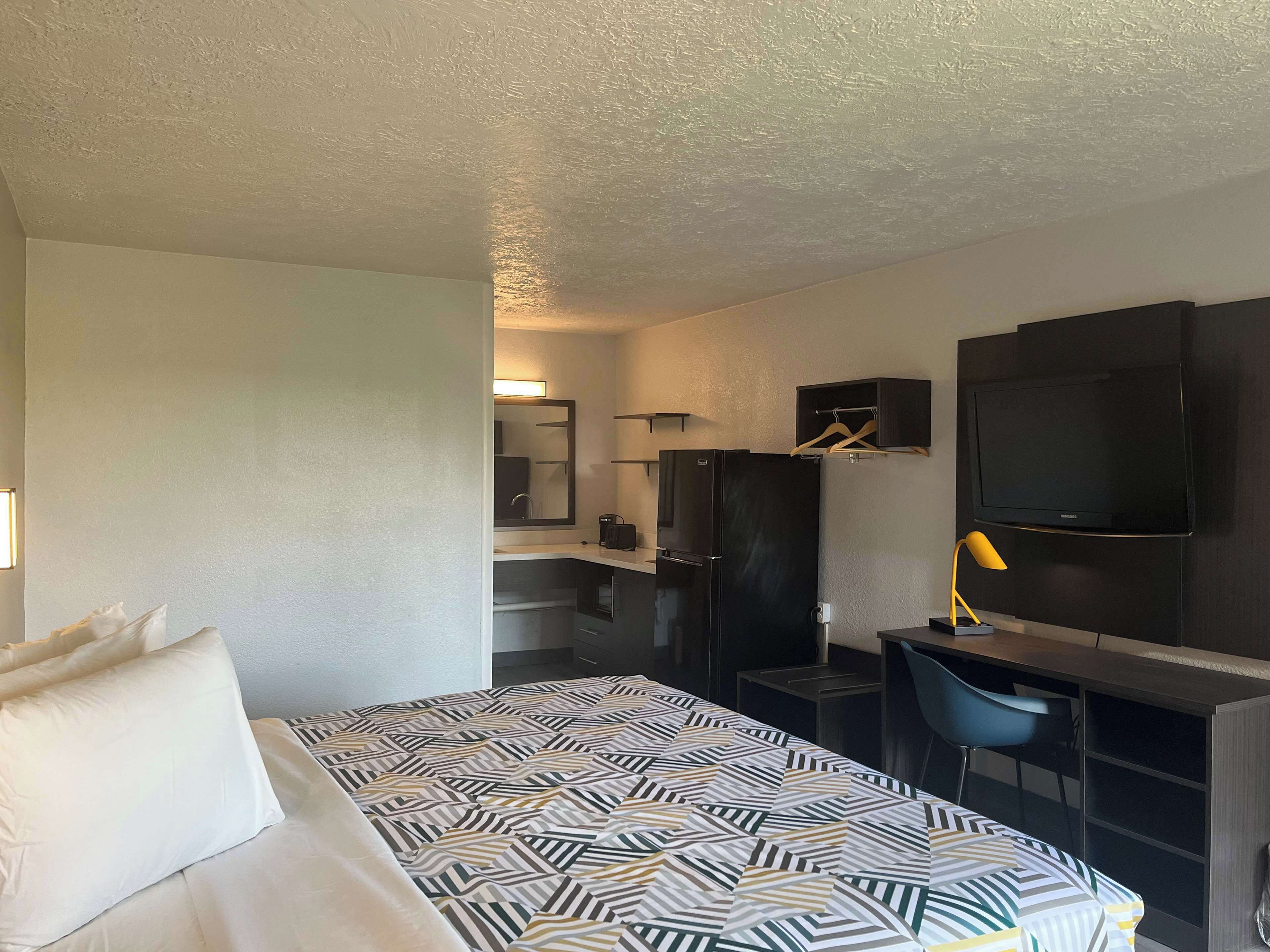 Una habitación de hotel con cama, escritorio, silla, televisor, espejo y armario.