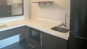 Eine moderne Küche mit dunklen Schränken, einer Edelstahl-Spüle und einem schwarzen Kühlschrank.