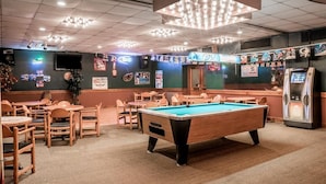 Ein Billardtisch in einem Raum mit mehreren Tischen und Stühlen, einem Jukebox und Sportmemorabilien an den Wänden.