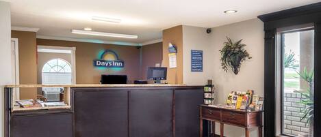 A reception area with a 'Days Inn' sign, a reception desk, a computer, a small table with brochures, and a window with blinds.