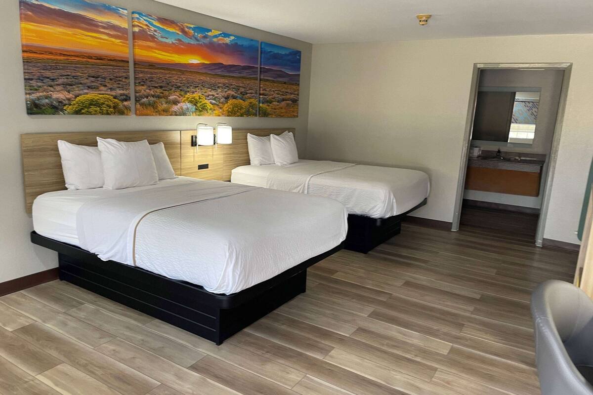A hotel room with two beds, a wooden floor, and a large landscape painting above the beds.