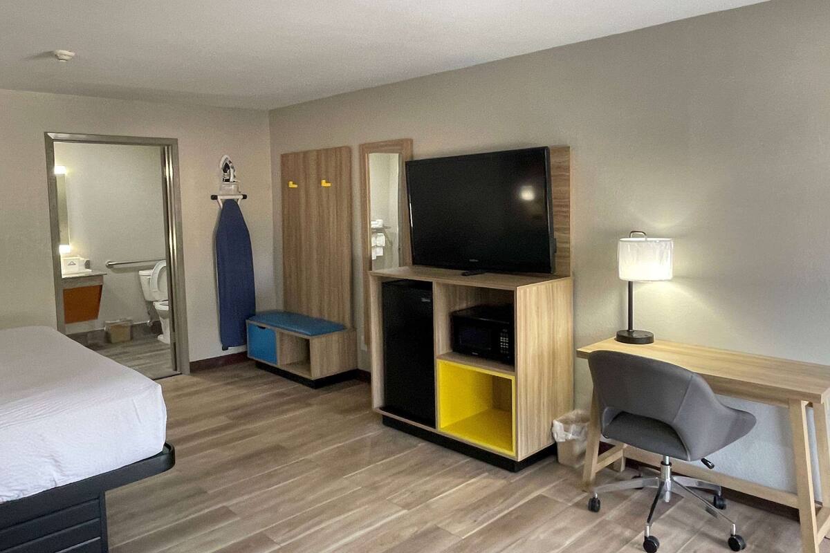 A hotel room with a bed, a desk with a chair, a television, a wardrobe, and a mirror.