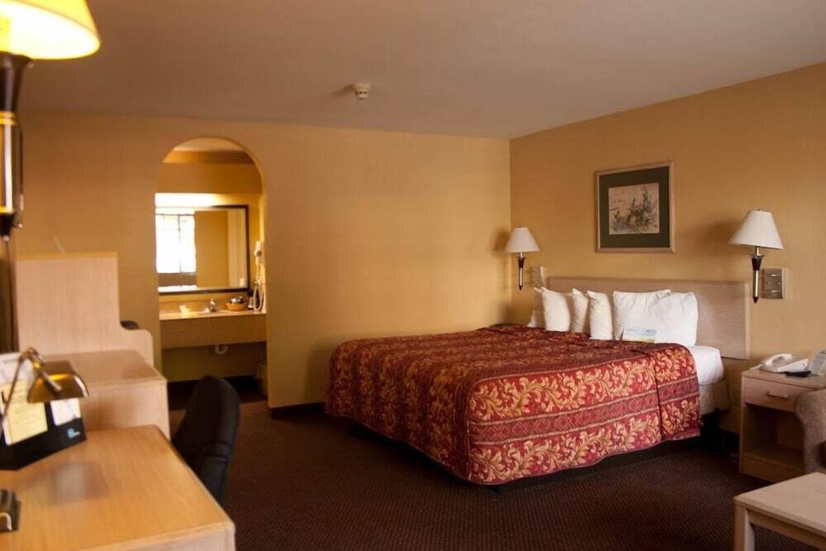 A hotel room with a bed, desk, chair, and a mirror.