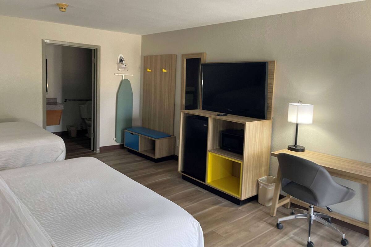 A hotel room with two beds, a desk with a chair, a television, and a small seating area.