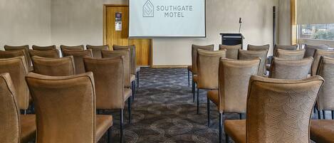 A conference room with a projector screen displaying the Southgate Motel logo, arranged seating, and a carpeted floor.