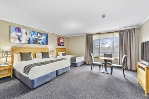 Habitación de hotel con dos camas, un escritorio con silla, televisión y obras de arte en las paredes.
