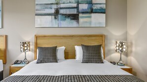 Cama bem arrumada com almofadas estampadas, cabeceira de madeira e duas luminárias de mesa.