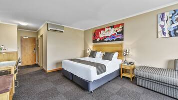 Een hotelkamer met een groot bed, een nachtkastje met lamp, een stoel en een schilderij aan de muur.