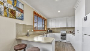 Uma cozinha moderna com armários brancos, forno embutido e um espaço bar com banquetas.