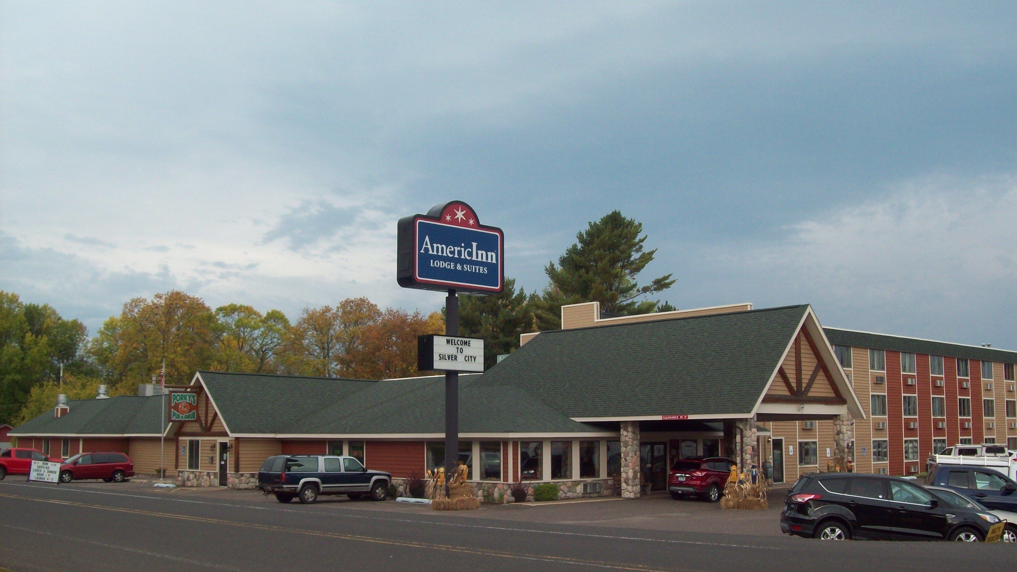 Un motel con un letrero de AmericInn, un cartel de bienvenida a Silver City y un restaurante visible llamado Porky's.