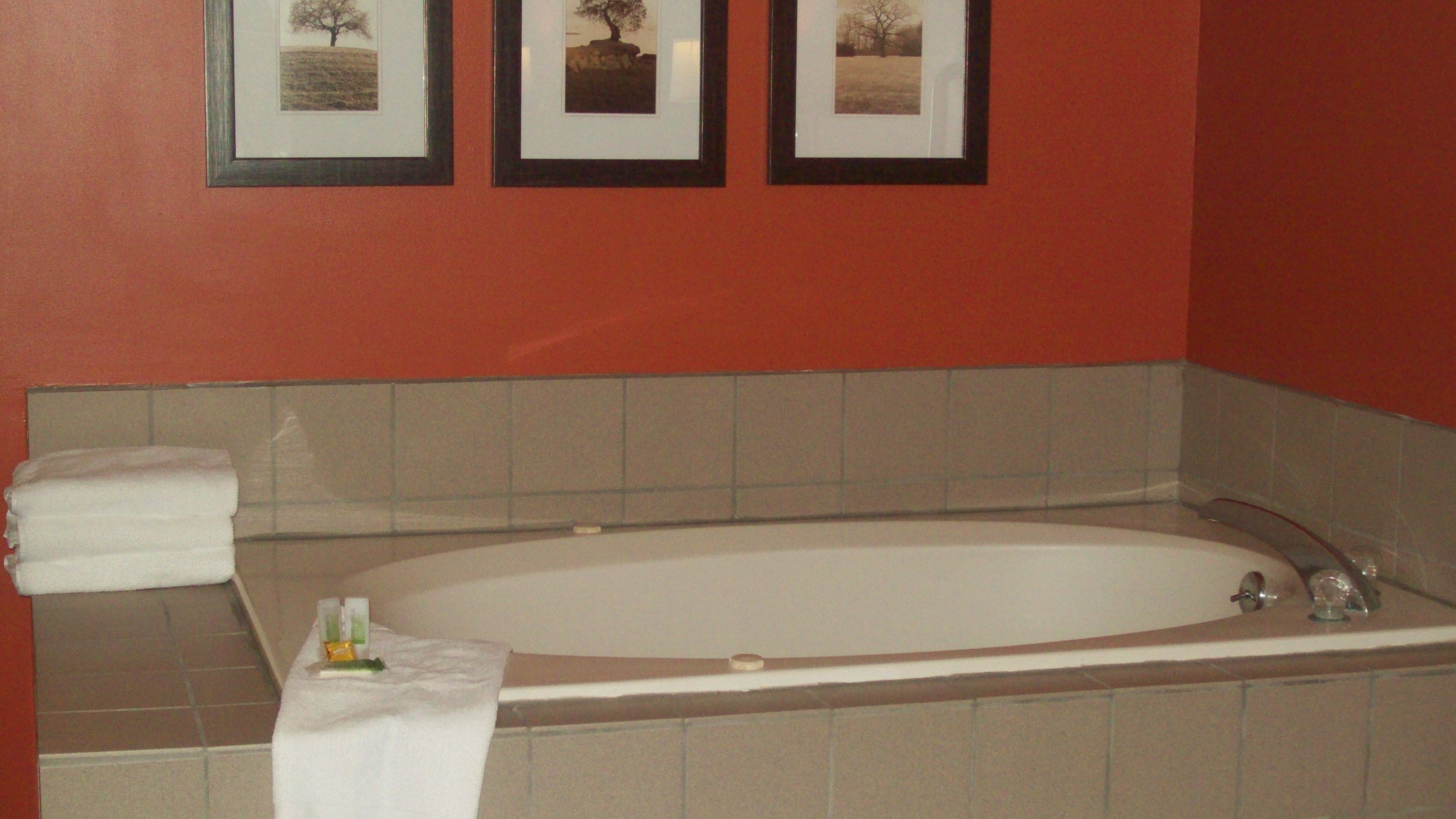 Een badkamer met een bad, een handdoek en drie foto's in lijsten aan de muur.