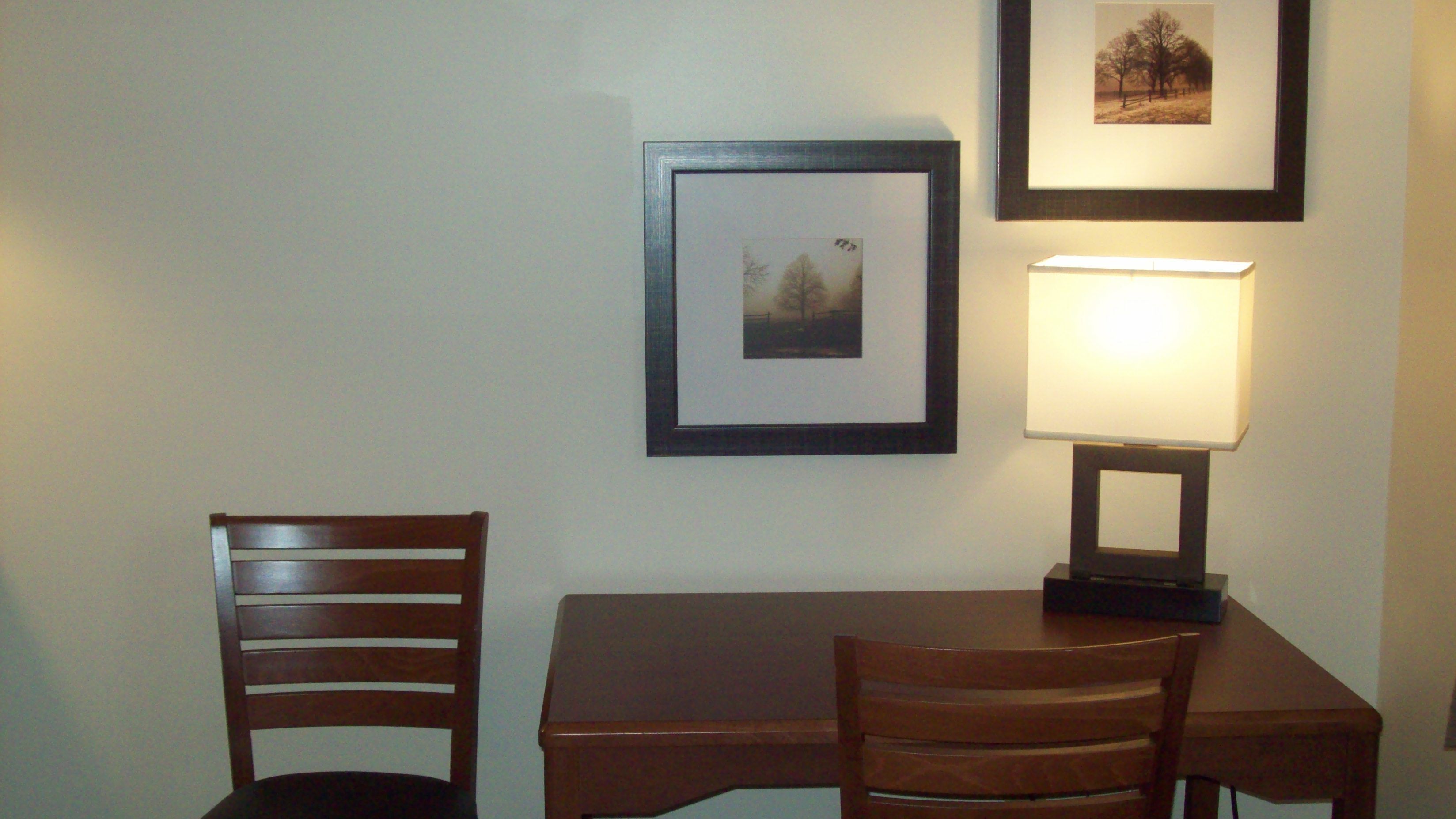 Un pequeño comedor con una mesa y dos sillas, un cuadro en la pared y una lámpara de mesa.