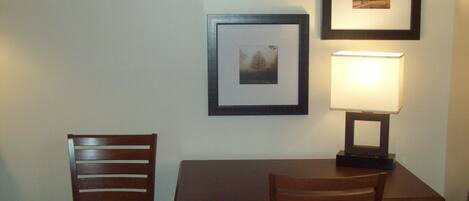 Un pequeño comedor con una mesa y dos sillas, un cuadro en la pared y una lámpara de mesa.