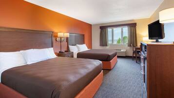 A hotel room with two beds, a desk with a television, and a window with curtains.