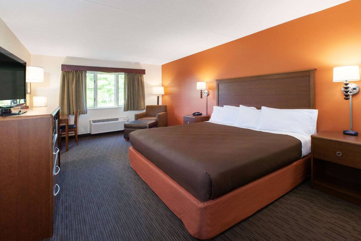 Ein Hotelzimmer mit einem großen Bett, einem Schreibtisch mit Fernseher, einem Sessel und zwei Nachttischlampen.