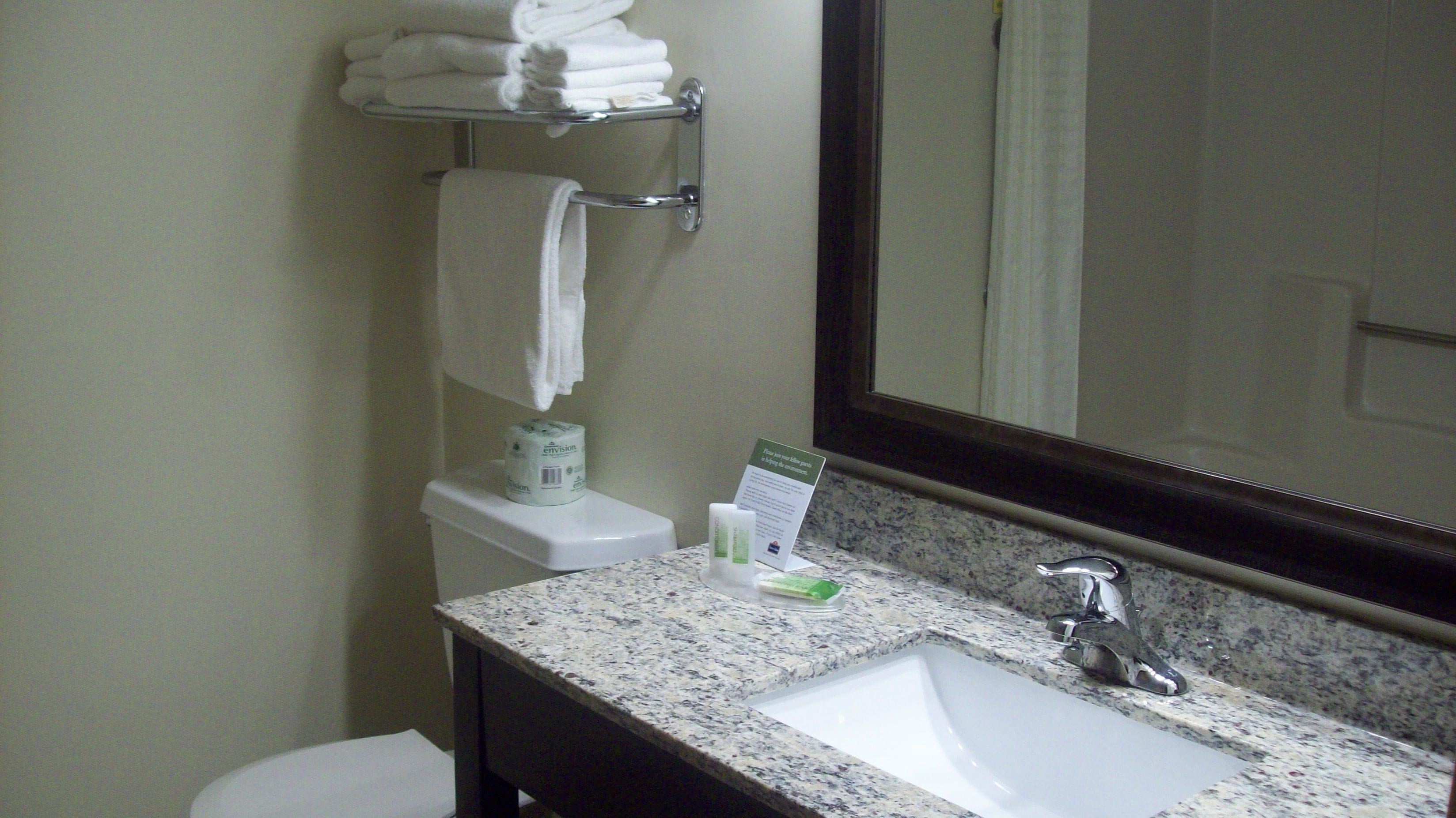 A bathroom with a sink, mirror, towel rack, toilet, and a toilet paper dispenser.