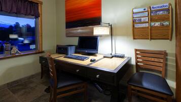 A hotel room with a wooden desk, two chairs, a computer, and a lamp. There is a window with a view of the outside.