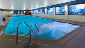 Een binnenzwembad met vrij uitzicht op de zee door grote ramen, een zwemplatform en enkele stoelen en tafels in de buurt van het zwembad.