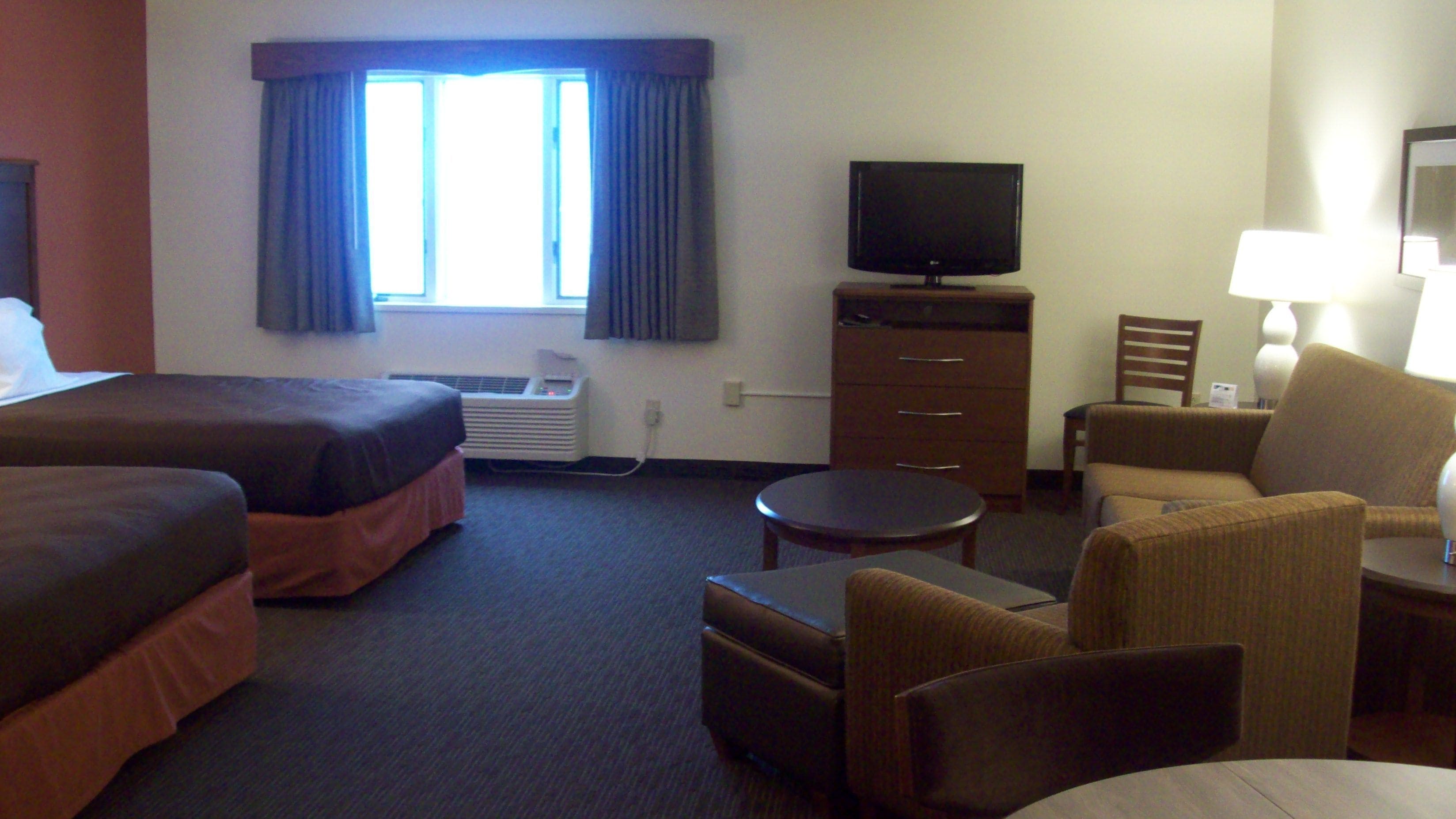 A hotel room with two beds, a TV, a desk with a lamp, a chair, and a small table.