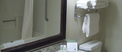 A bathroom with a shower, a sink with a marble countertop, a towel rack with folded towels, and a sign about environmental conservation.