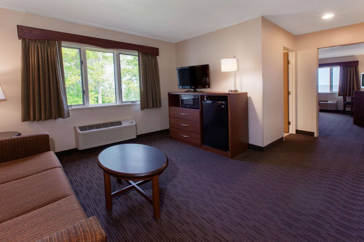 Ein Hotelzimmer mit einer Sitzecke, einem kleinen Tisch, einem Fernseher, einer Mikrowelle, einer Lampe und einem Fenster mit Vorhängen.