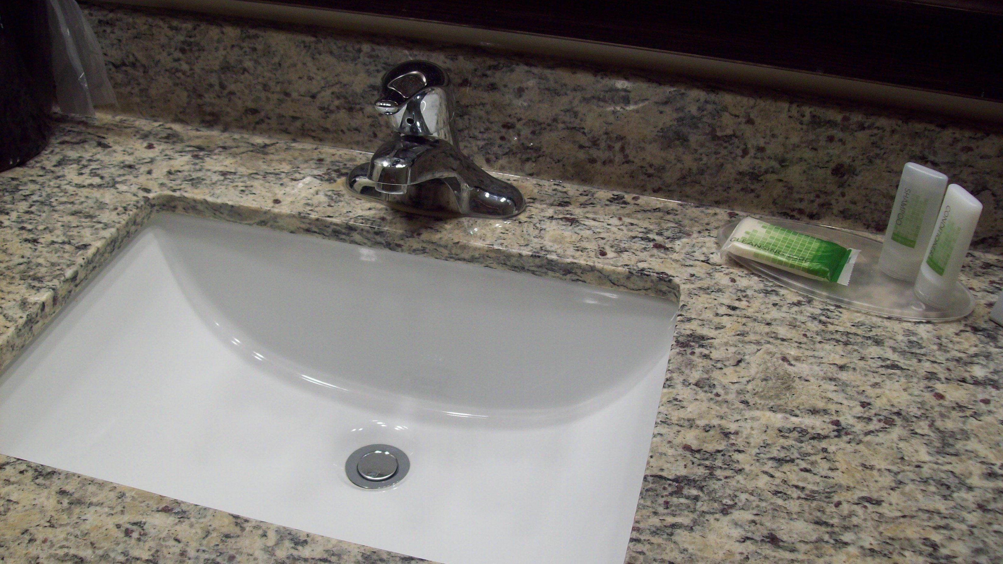 A white sink with a single faucet, a soap dispenser, and a hand soap container on a granite countertop.