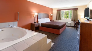 Een hotelkamer met een groot bad, een bed met een bruine hoofdeinde, een bureau met een televisie, en een raam met gordijnen.