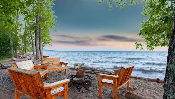 Een houten terras met Adirondack stoelen en een vuurkuil aan het strand.