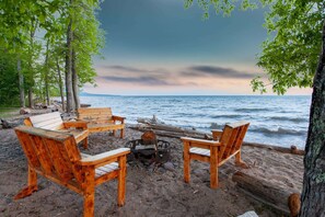 Eine Holzterrasse mit Adirondack-Stühlen und einem Feuerkorb am Strand.