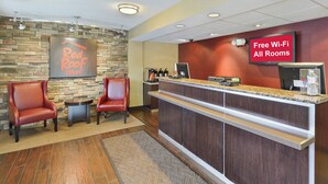 L’espace d’accueil d’un hôtel Red Roof Inn, avec un mur en pierre, deux fauteuils en cuir, un comptoir d’accueil et un panneau indiquant que le Wi-Fi est gratuit dans toutes les chambres.