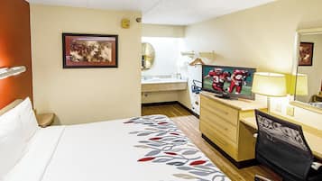 Habitació d'hotel amb un llit, una taula de treball amb cadira, televisió, mirall i un bany al fons.