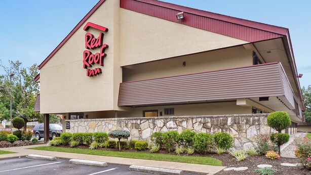 Un hôtel Red Roof Inn avec une façade en pierre, un toit en pente et un parking.