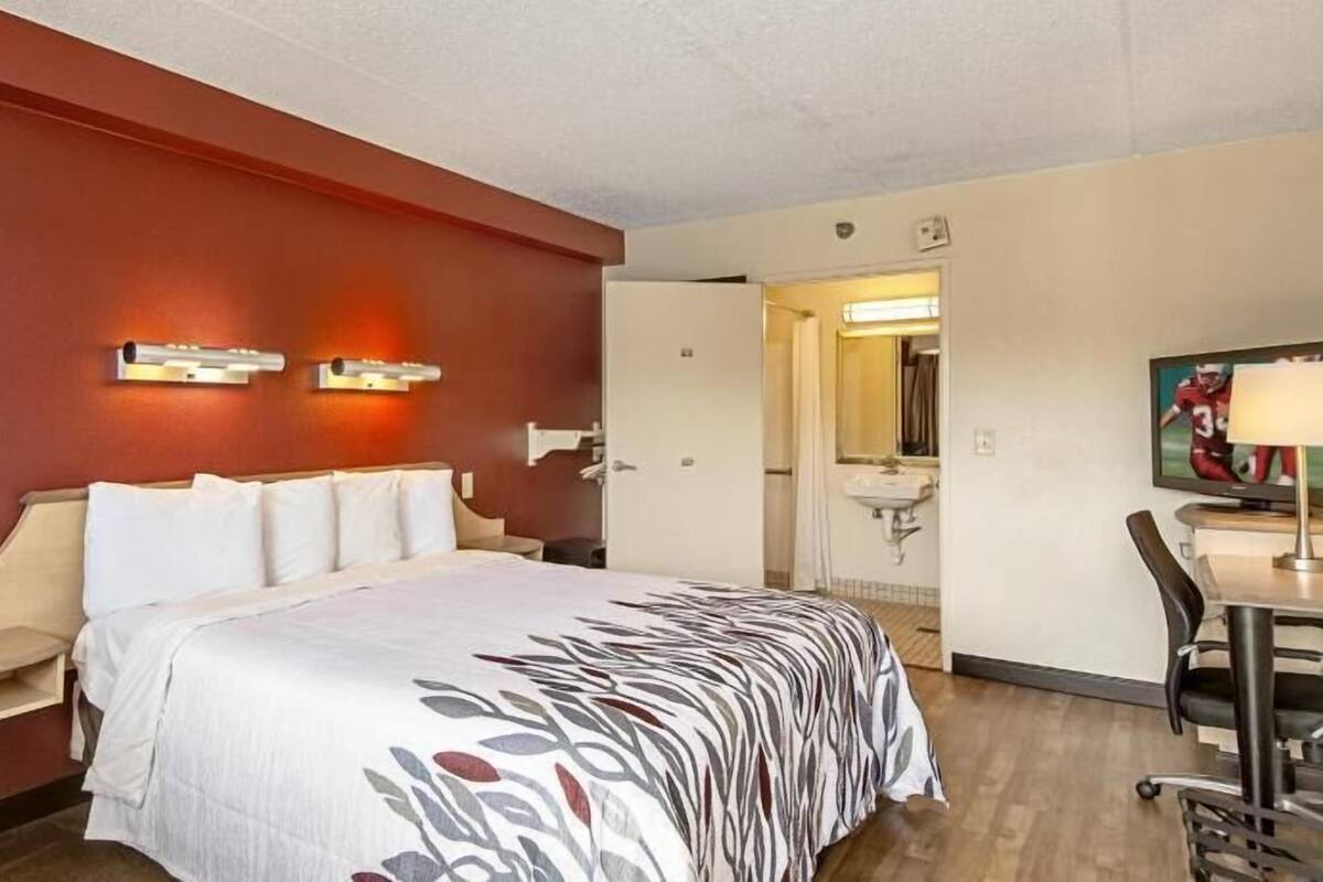 Une chambre d’hôtel avec un lit, un bureau et une chaise, un téléviseur et une salle de bain visible à travers une porte ouverte.