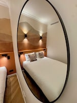 A bedroom with a bed, two wall-mounted lights, and a mirror reflecting the room.