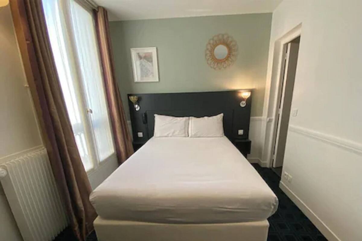 A hotel room with a large bed, a nightstand, a wall-mounted mirror, and a door.