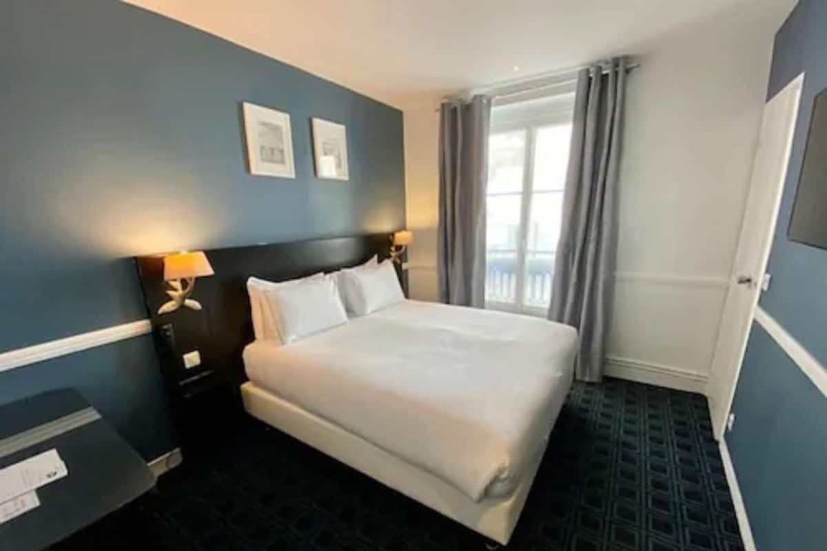 A hotel room with a large bed, a nightstand, a lamp, and a window with curtains.
