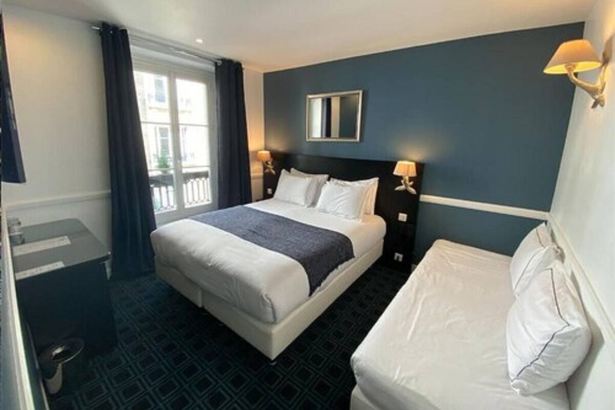 A hotel room with a large bed, a smaller bed, a window with curtains, and a wall-mounted mirror.