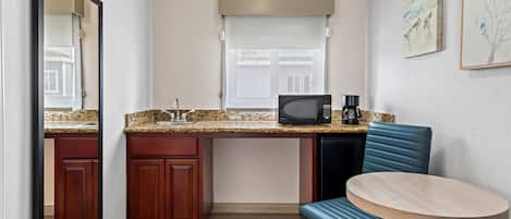 A compact kitchen with a microwave, coffee maker, and a dining area with a chair and table.