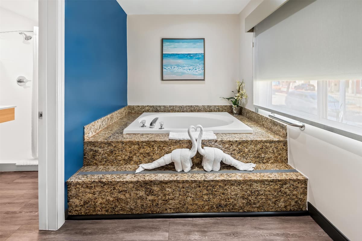 Ein modernes Badezimmer mit einer Granitplatte, einer Badewanne, einem Bilderrahmen mit einem Strandmotiv und einem Fenster mit Blick.