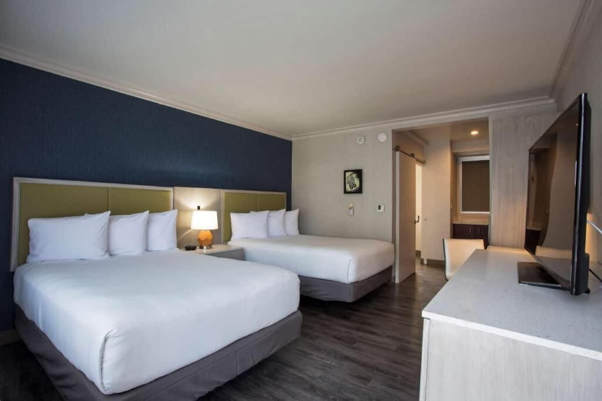 Ein Hotelzimmer mit zwei Betten, einem Schreibtisch, einem Fernseher und einer Tür zu einem Badezimmer.