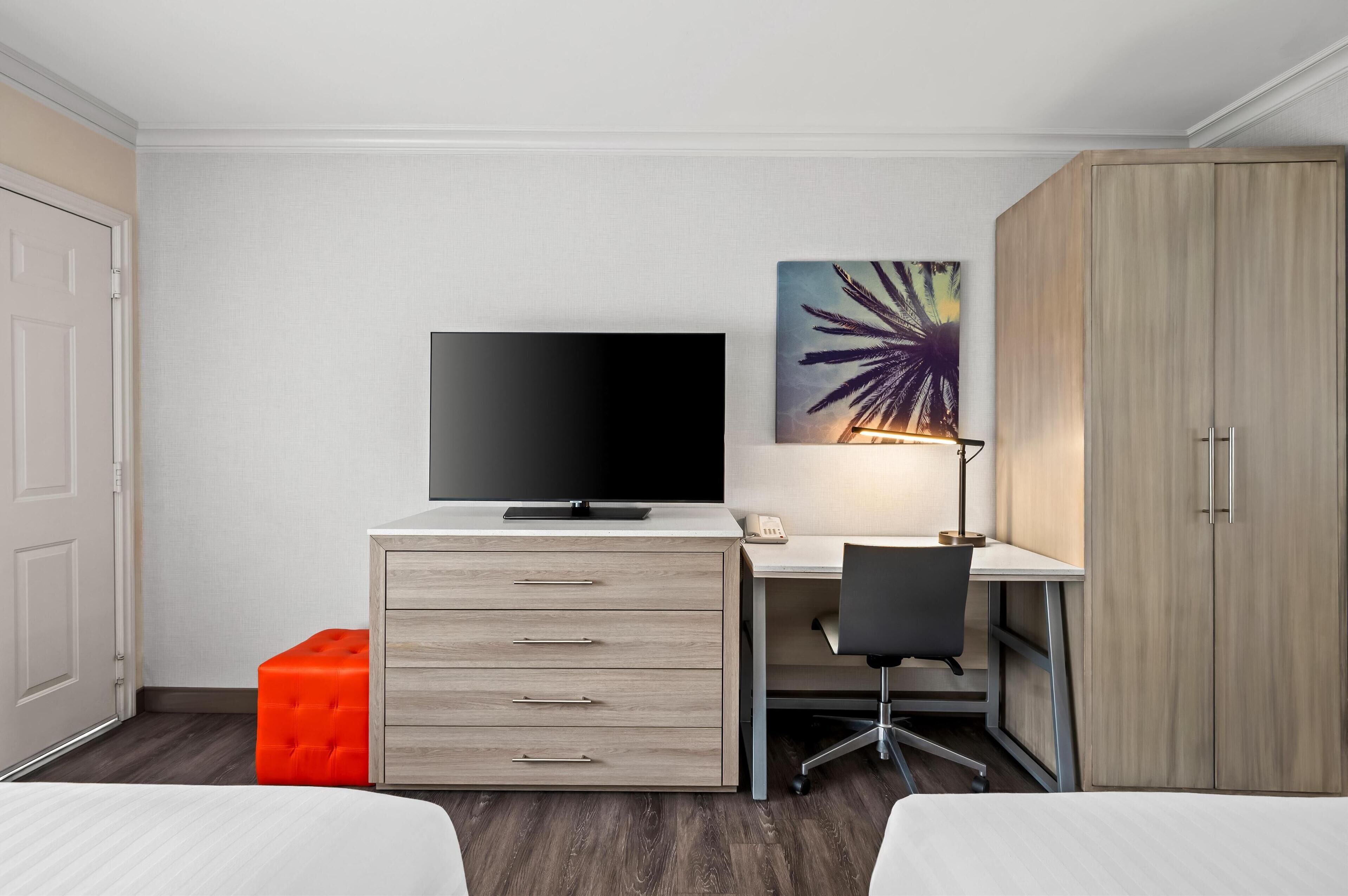 A hotel room with a bed, a desk with a computer, a television, and a wardrobe.