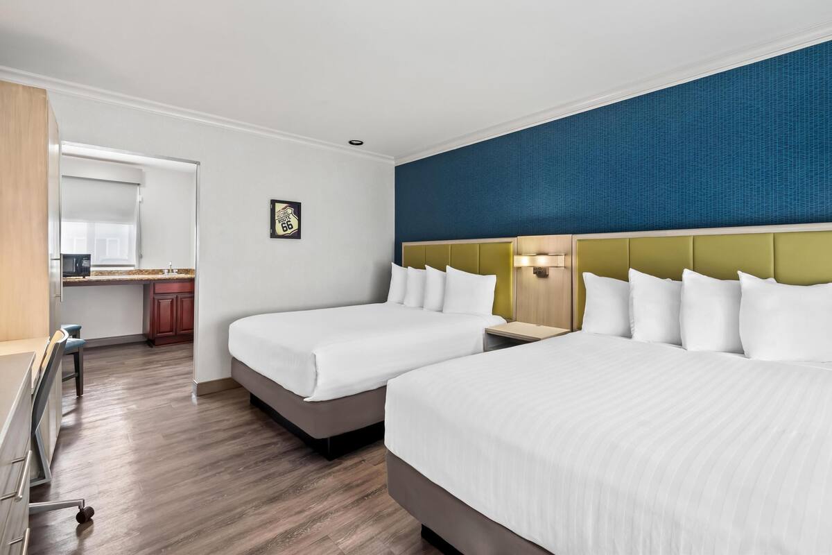 Ein Hotelzimmer mit zwei Betten, einer Küchenzeile und einer blauen Akzentwand.