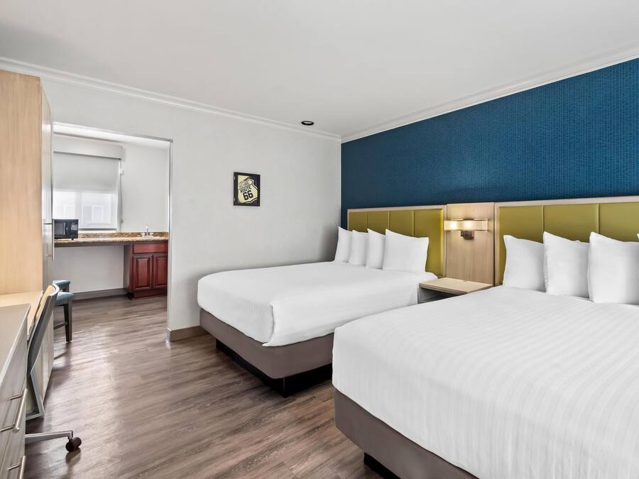 Habitación de hotel con dos camas, kitchenette y una pared azul de acento.