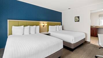 A hotel room with two beds, a nightstand, a wall clock, and a small kitchen area.