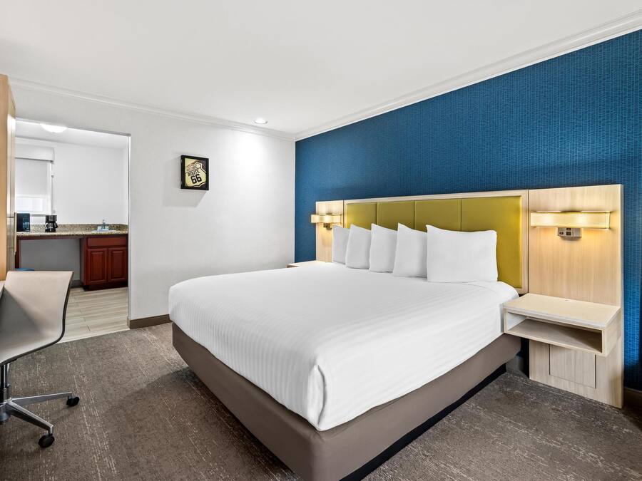 A modern hotel room with a large bed, a desk, and a kitchenette.