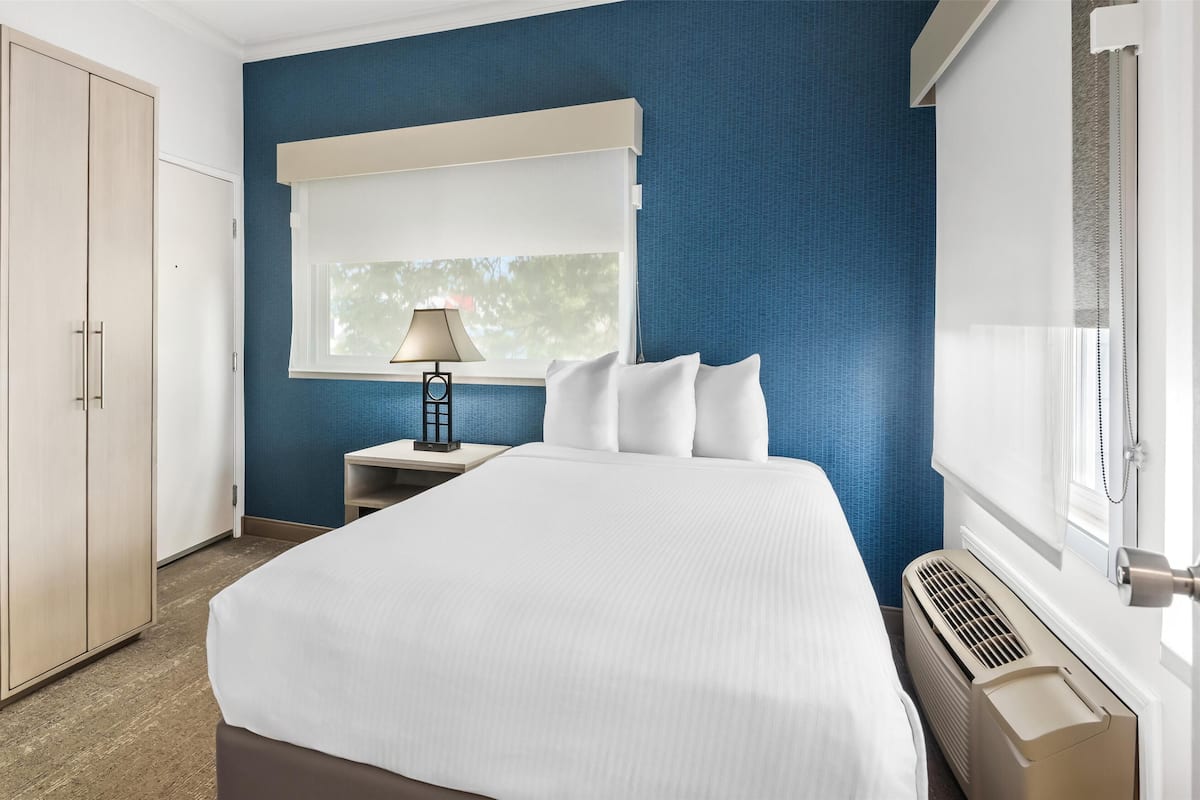 Ein Hotelzimmer mit einem großen Bett, einem Nachttisch mit Lampe, einem Kleiderschrank und einem Fenster mit Jalousien.