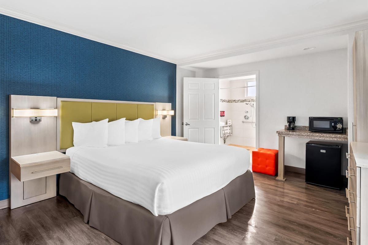 Ein Hotelzimmer mit einem großen Bett, Nachttischen, einer kleinen Küchenzeile und einem durch eine offene Tür einsehbaren Badezimmer.